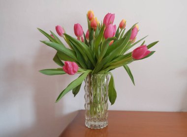 Vazoda renkli lalelerle dolu bir buket. Ahşap çekmecede, beyaz duvarın karşısında. Uzayı kopyala İç dekorasyon. Otel odası.