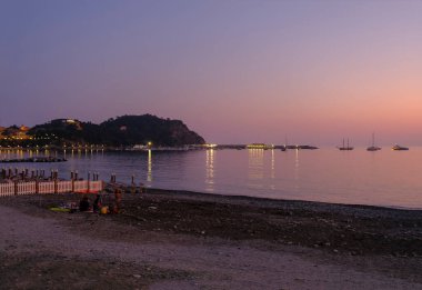 Sestri Levante, Liguria, İtalya 'da gün batımında kıyı şeridi ve şehir silüeti. Şehir arka planı, denizdeki tekne ve otellerin yansımaları.