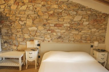 Taşlardan ve beyaz mobilyadan yapılmış bir duvarı olan bir otel odasının içinde.. 