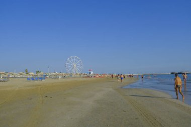 Temmuz 2023 Rimini, İtalya: Ufuk ve dönme dolap boyunca uzanan Rimini plajı ve eğlenen insanlar