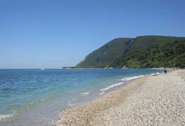 Sunny day at the pebbles beach across the cliffs in Marche, Italy. Coastline, horizontal line, natural background. turquoise water
