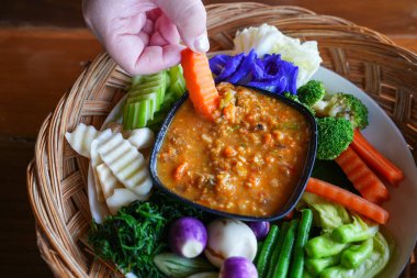 Bir el biber ezmesini taze sebzeye batırıyor.