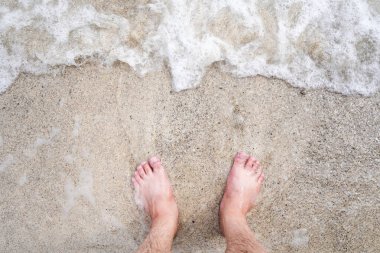 Sahilde ve denizde çıplak ayaklı bir adam.