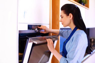 Güzel genç bayan pastasının fırında ne yaptığını kontrol ediyor..