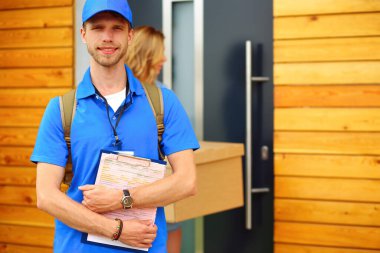 Mavi üniformalı gülümseyen kurye servis konseptine paket kutusu teslim eden teslimatçı. Mavi üniformalı gülümseyen teslimatçı..