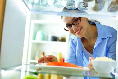 Sağlıklı yiyecek, sebze ve meyvelerle dolu açık buzdolabının yanında duran kadın portresi.