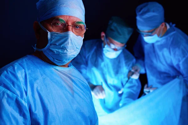 Group of surgeons at work in operating theater toned in blue. Medical team performing operation.