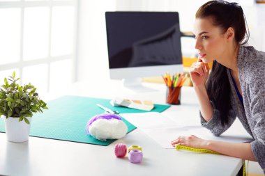 Moda tasarımcıları stüdyoda çalışıyor, masanın yanında duruyorlar..