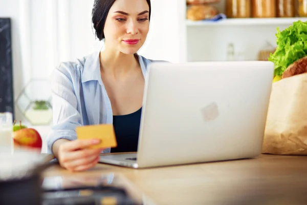 キッチンでコンピュータやクレジットカードを使用して笑顔の女性オンラインショッピング — ストック写真
