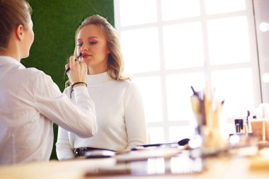 Makyaj sanatçısı, mankenlerin gözüne beyaz göz farı sürüyor ve arka planda göz farı olan bir kabuk tutuyor..