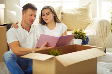 Genç çift yeni evde yerde otururken albüm tutuyor..