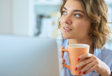 Ofis masasında oturan çekici bir kadın elinde bir fincan kahve tutuyor..