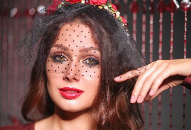 Siyah peçeli, saçlarında kırmızı çiçekler olan romantik, modaya uygun bir kadın..