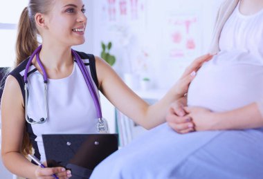 Steteskoplu ve tabletli genç kadın doktor hastanede hamile bir kadınla konuşuyor.
