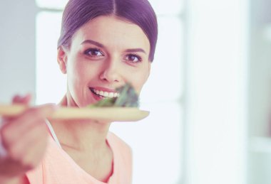 Gülümseyen genç kadın mutfakta taze salata karıştırıyor..