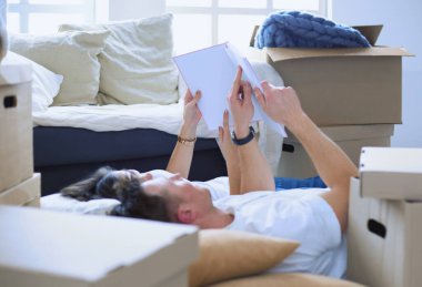 Yeni evlerinde karton kutuları açıp yere uzanan ve bir aile albümüne bakan sevimli çift.