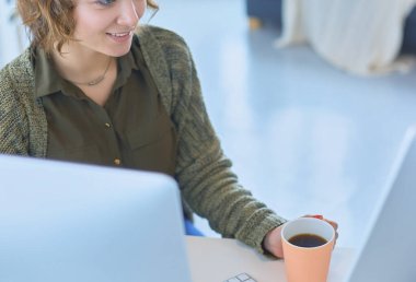 Ofis masasında oturan çekici bir kadın elinde bir fincan kahve tutuyor..