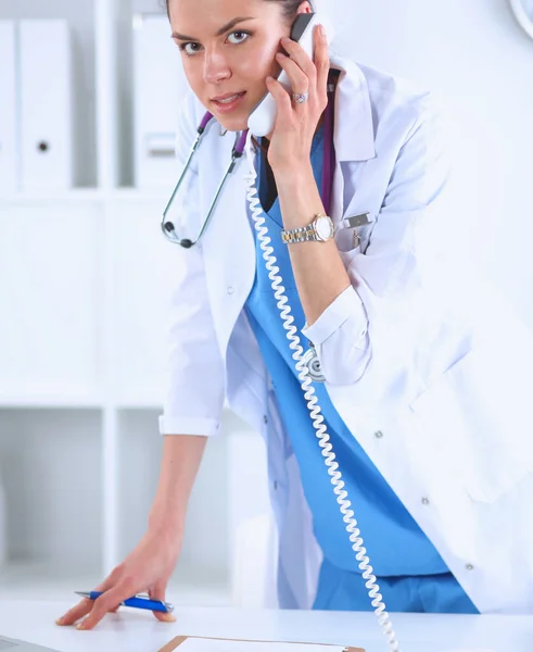 携帯電話を使用してコンピュータで白いコートの若い女性医師の肖像画 — ストック写真