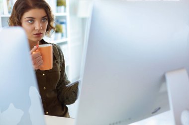 Ofis masasında oturan çekici bir kadın elinde bir fincan kahve tutuyor..