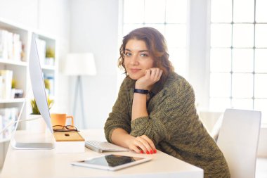 Evdeki bir masada birden fazla cihaz kullanarak çalışan mutlu kadın..