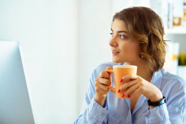 迷人的女人坐在写字台前 手里拿着一杯咖啡 — 图库照片
