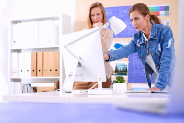 Masanın yanında duran iki genç kadın enstrüman, plan ve dizüstü bilgisayarla.