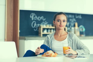 Mutfakta portakal suyu ve tableti olan genç bir kadın..