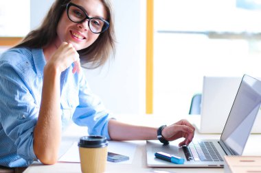 Dizüstü bilgisayar ekranına bakarak office tablosunda oturan genç kadın .