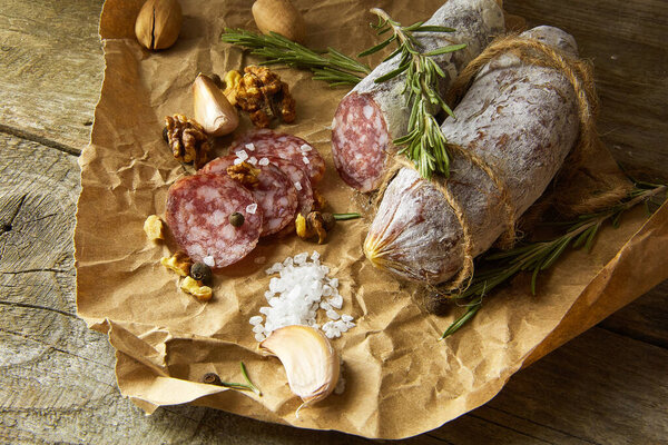 Italian salami wih sea salt, rosemary, garlic and nuts on paper. Rustic style. Top view.