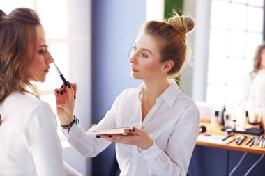 Makyöz, genç bir kadının profesyonel makyajını yapıyor..