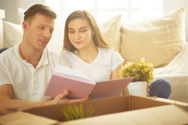 Genç çift yeni evde yerde otururken albüm tutuyor..