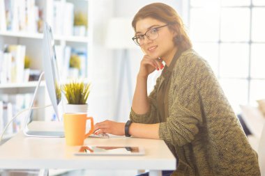 Evdeki bir masada birden fazla cihaz kullanarak çalışan mutlu kadın..
