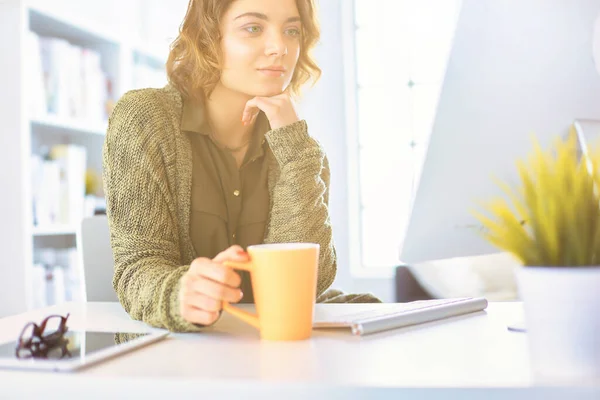 一个迷人的微笑的女人坐在写字台前 端着一杯咖啡 她正在放松地看着远方 — 图库照片