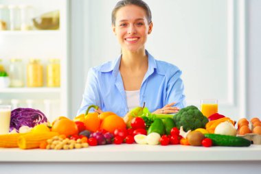 Ahşap iç kısımda meyve ve sebze dolu masada oturan genç ve tatlı bir kadın.