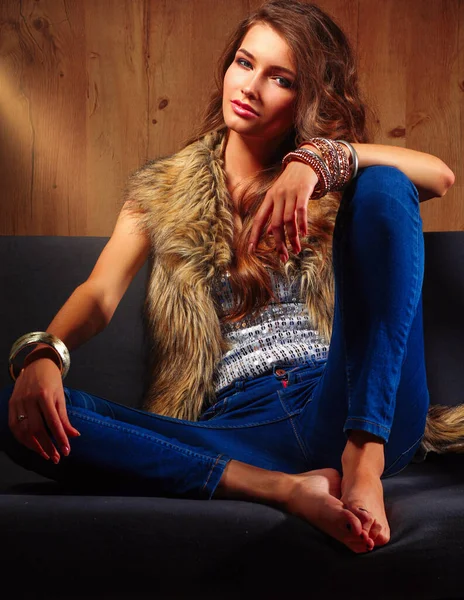 穿着毛皮外套坐在沙发上的年轻漂亮的时尚女人 — 图库照片