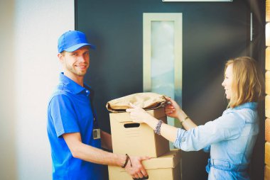 Mavi üniformalı gülümseyen kurye servis konseptine paket kutusu teslim eden teslimatçı. Mavi üniformalı gülümseyen teslimatçı..