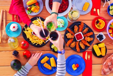 Ahşap masada otururken birlikte yemek yiyen bir grup insanın üst düzey görüntüsü. Masada yemek var. İnsanlar fast food yiyor.