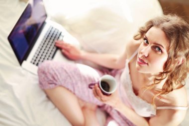 Dizüstü bilgisayar ile yatakta oturan genç güzel kadın