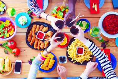 Ahşap masada otururken birlikte yemek yiyen bir grup insanın üst düzey görüntüsü. Masada yemek var. İnsanlar fast food yiyor..