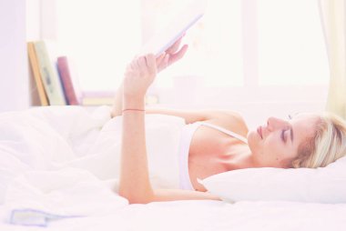 Elinde boş ekranlı dijital tablet tutan ve yatak odasında kameraya gülümseyen bir kız..