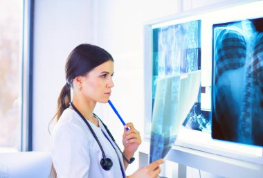 Doktor muayenehanesinde röntgene bakan steteskoplu, gülümseyen genç bayan doktor.