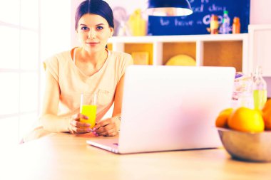 Mutfakta dizüstü bilgisayara benzeyen tariflerle gülümseyen genç bir kadın. Gıda blogcusu kavramı.