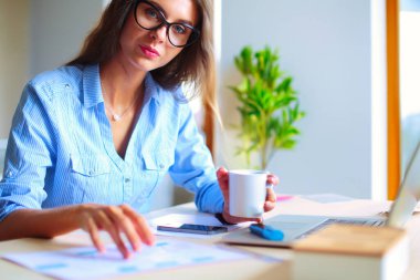 Ofis masasında oturan genç bir kadın dizüstü bilgisayar ekranına bakıyor. Genç kadın..