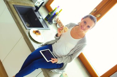 Mutfakta dijital tablet kullanan güzel genç bir kadın.