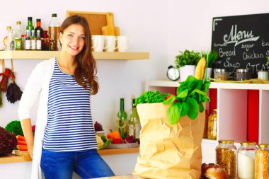 Bakkal alışveriş çantası sebzeli tutan genç kadın. Mutfakta ayakta. Genç kadın.