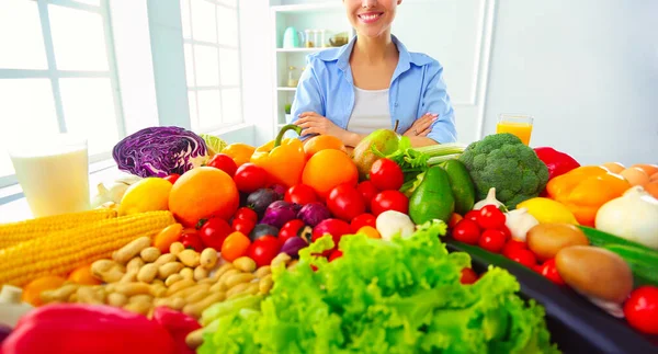 stock image Young and cute woman sitting at the table full of fruits and vegetables in the wooden interior.