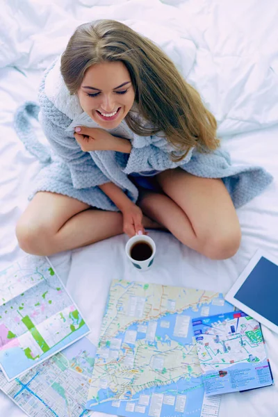 リラックスした若い女性がベッドの上にコーヒーとデジタルタブレットのカップで座っています — ストック写真