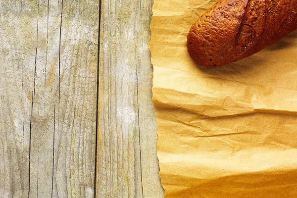 一块面包 用纸包在木制桌子上 — 图库照片