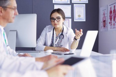 Ciddi bir tıbbi ekip parlak bir ofiste dizüstü bilgisayar kullanıyor..