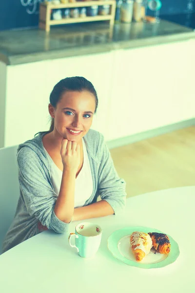 stock image Woman drinking tea with sweet croissant at the kitchen table.